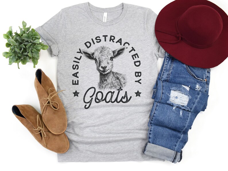 May include: A gray t-shirt with a black and white illustration of a goat and the text "Easily Distracted by Goats".