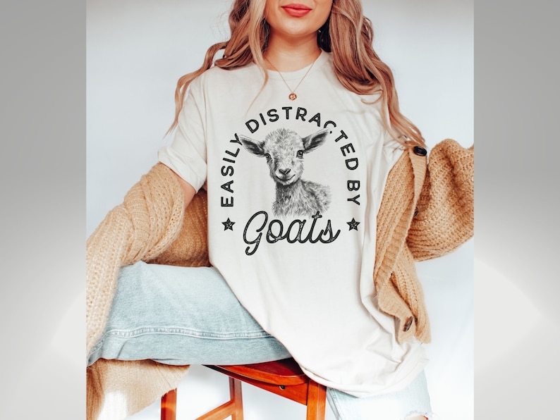 May include: A white t-shirt with a black and white illustration of a goat and the text "Easily Distracted by Goats" printed on the front.