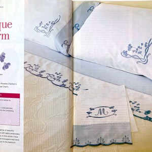 White pillowcases and sheets set on a bed. The pillowcases and sheets have blue edging and embroidered monograms.