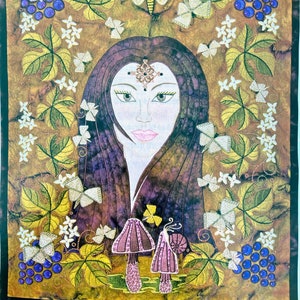 An embellished wallhanging featureing the image of a young woman with long brown hair surrounded by grapevines, white flowers and butterflys. At the base are two toadstools on which a snail sits. At the bottom of the hanging is the word Autumn.