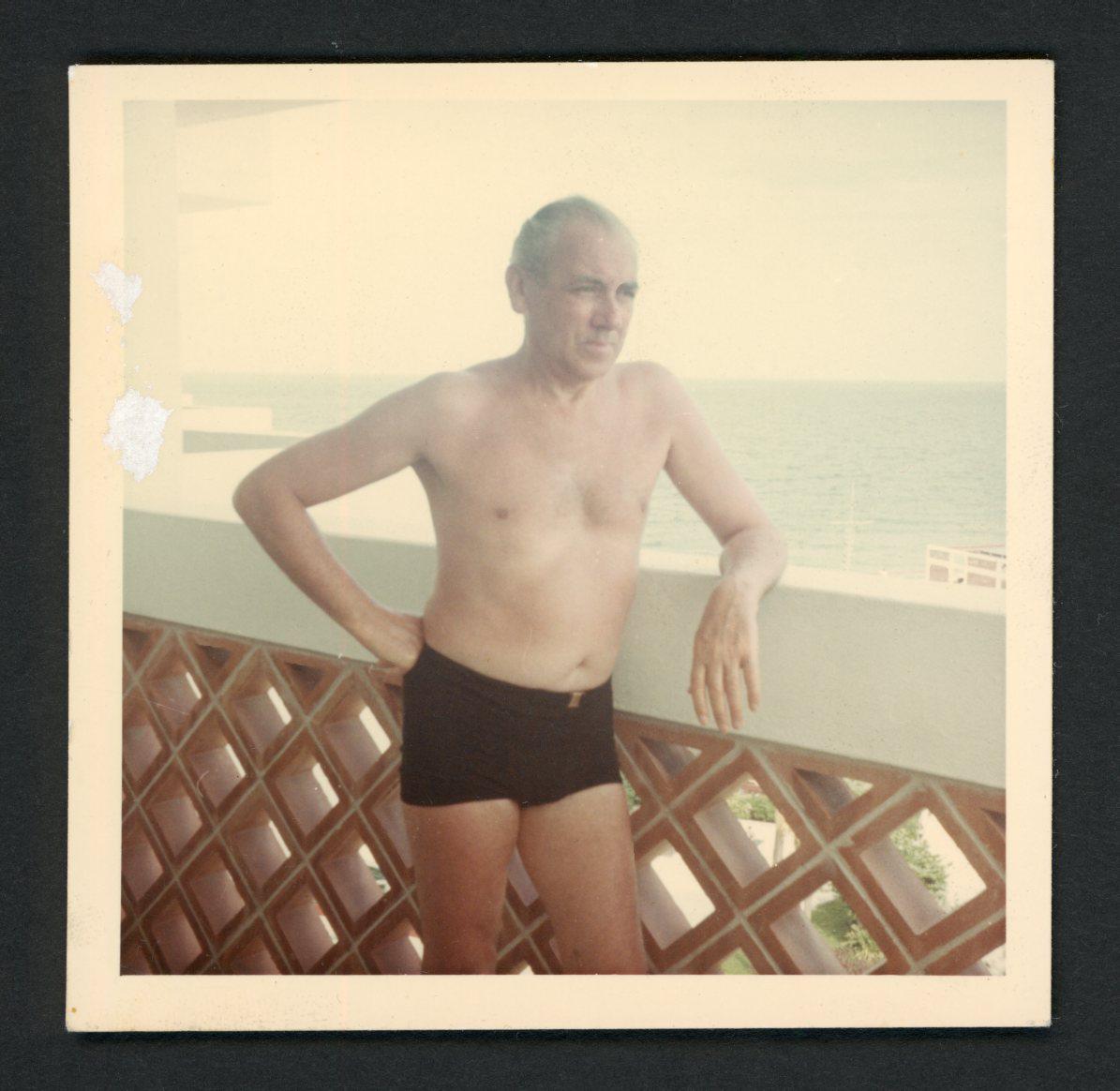 Vintage fotomomentopname jaren 60: knap shirtloos mannenbadpak leunt op zeehek