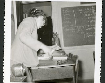 Vintage foto uit de jaren 1950: vrouw aan een schoolbankje voor een schoolbord.