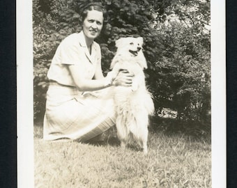 Vintage foto uit de jaren 1930: vrouw knielt naast een klein, harig hondje dat op zijn achterpoten staat.
