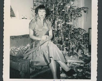 Vintage vierkante foto uit de jaren 1950. Elegante vrouw zit naast een fonkelende kerstboom in de woonkamer, versierd met slingers en een tv.