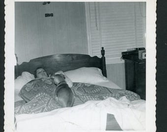 Fotografía vintage de los años 60: Perro pequeño encima de un niño en la cama. Mascotas: cachorros. Interior.