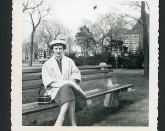 Stilvolle Frau auf einer Parkbank, gekleidet für den Ostersonntag, Kleid, Hut, Mantel, Handtasche, quadratisches Vintage-Foto, Schnappschuss, Mode der 1950er Jahre, Mitte des Jahrhunderts