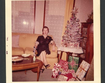 Vintage foto uit de jaren 60: elegante vrouw in cocktailjurk zittend bij een kerstboom met slingers, interieurdecoratie uit het midden van de 20e eeuw.