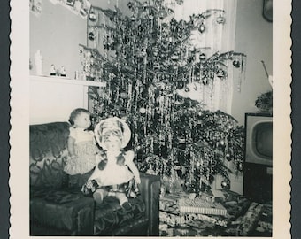 Vintage vierkante foto uit de jaren 50: een sprankelende kerstboom met een display van babypoppen en speelgoed, een tv met slingers in de woonkamer.
