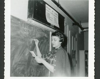 Vintage foto uit de jaren 50: een lerares schrijft op een schoolbord in een klaslokaal. Interieur uit het midden van de 20e eeuw.