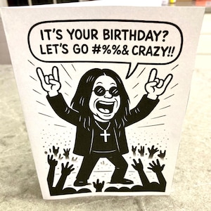 May include: A black and white birthday card featuring a cartoon illustration of a rock star with long hair, sunglasses, and a cross necklace. The card reads "IT'S YOUR BIRTHDAY? LET'S GO #%&%& CRAZY!!" with a crowd of hands in the background.