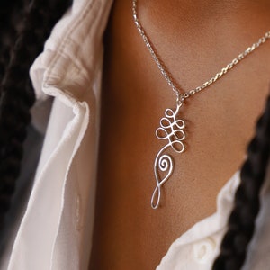 May include: A silver chain necklace with a delicate, abstract pendant. The pendant is made of twisted wire and has a flowing, organic shape.