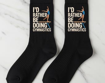 May include: A pair of black crew socks with the text "I'D RATHER BE DOING GYMNASTICS" in white and a gymnast illustration. The socks feature a ribbed design and are made of a soft, comfortable material.