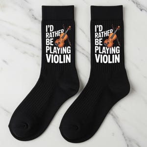May include: Pair of black socks with the text "I'D RATHER BE PLAYING VIOLIN" in white, along with a graphic of a violin. The socks are ribbed and likely made of a comfortable material.