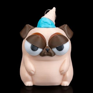May include: A 3D-printed pug figurine with a grumpy expression, wearing a blue party hat and a cone-shaped accessory. The pug is light tan with brown accents and large, expressive eyes. The background is black.