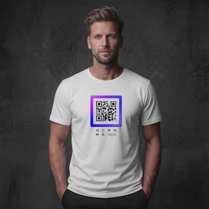 Könnte beinhalten: Ein weißes Kurzarm-T-Shirt mit einer quadratischen QR-Code-Grafik mit violett-blauem Farbverlauf. Unter dem QR-Code steht der Text "SCAN ME" in schwarzen Großbuchstaben, mit kleinerem Text unter dem Wort "ME".