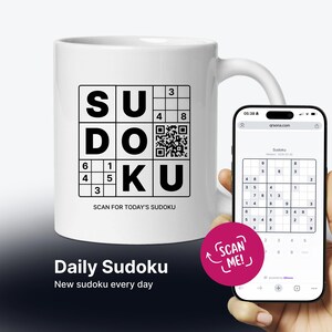 May include: A white ceramic mug featuring a black Sudoku grid design with the letters S, U, D, O, K, U integrated into the puzzle, a QR code, and the text SCAN FOR TODAY'S SUDOKU. A smartphone displays a digital Sudoku puzzle on its screen.