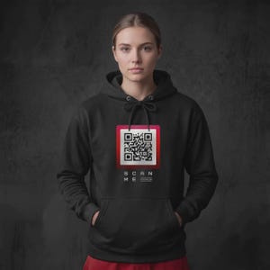 Peut inclure: Un sweat-shirt à capuche noir arborant un motif central composé d'un QR code à bordure rouge surmontant le texte blanc SCAN ME. Ce vêtement est doté d'une poche kangourou à l'avant et de cordons de serrage noirs au niveau du col.