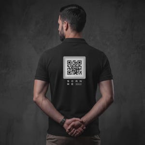 Könnte beinhalten: Ein schwarzes Poloshirt mit einer quadratischen weißen Grafik auf der Rückseite, die in der Mitte einen schwarzen QR-Code enthält. Unter dem QR-Code steht der Text "SCAN ME" in weißen Großbuchstaben, gefolgt von "QRCODE.COM".