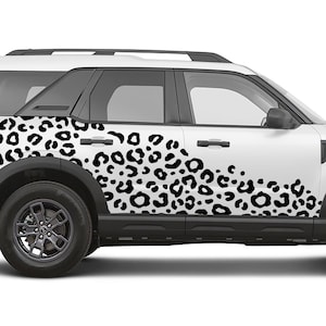 May include: White SUV featuring a black leopard print design on its side. The vehicle has black tyres and trim. The leopard print pattern consists of black spots on a white background.