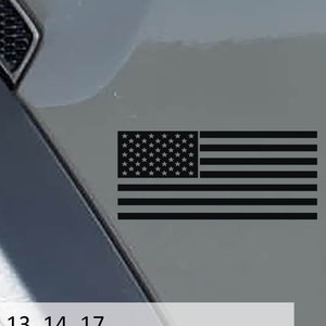 Puede incluir: Un adhesivo de bandera estadounidense en blanco y negro en un coche gris. La bandera está en la esquina inferior derecha de la imagen. El texto "Black - sRGB 13, 14, 17" está en la parte inferior de la imagen.