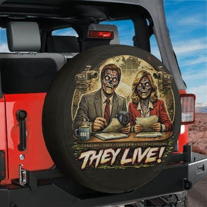 May include: Black spare wheel cover with a graphic from the film "They Live." The design shows zombie-like figures at a news desk, the word "OBEY" on a mug, and the phrase "THEY LIVE!" in large letters.