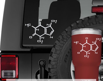Op de afbeelding: Een donkerrode roestvrijstalen beker met een witte grafische weergave van de moleculaire structuur van cafeïne en de merknaam YETI onderaan. Dezelfde witte chemische formule is als sticker op een donker voertuigraam afgebeeld.