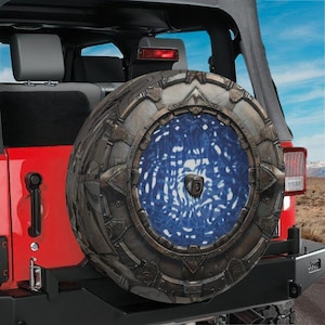 May include: A circular spare tire cover mounted on the back of a red vehicle. The cover features a graphic design of a metallic, mechanical ring structure surrounding a swirling, textured blue and white portal-like center with a camera lens.