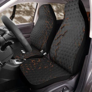 May include: Black car seat covers with a geometric honeycomb pattern and orange accents. The covers are designed to fit the front seats of a vehicle. The steering wheel is visible in the image.