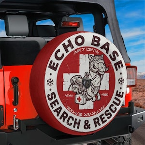 Puede incluir: Funda de neumático de repuesto roja y blanca con texto "ECHO BASE SEARCH & RESCUE" y un gráfico de criatura de dibujos animados. La funda está montada en un Jeep rojo. El diseño incluye copos de nieve y una cruz.