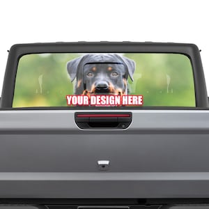 May include: A black and tan Rottweiler dog looking out of the rear window of a grey pickup truck. The window has a custom design with the text "YOUR DESIGN HERE".