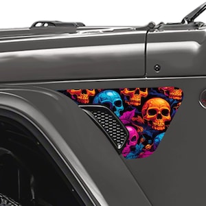 May include: A triangular vehicle decal applied to the side panel of a gray car. The decal features a vibrant, multi-colored pattern of skulls in shades of orange, blue, and pink, interspersed with dark foliage elements against a black background.