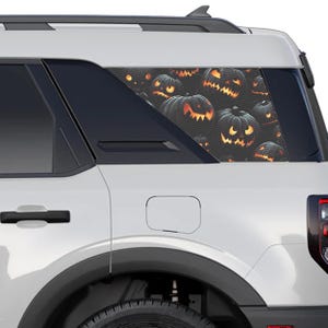 Peut inclure: Un SUV blanc avec un autocollant de citrouilles en forme de jack-o'-lantern noires et orange sur la vitre arrière. Les citrouilles sont disposées de manière aléatoire et ont un thème d'Halloween effrayant.