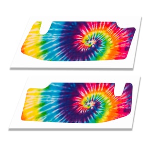 May include: Two identical visor-shaped decals featuring a vibrant tie-dye pattern with a central spiral design. The colours include bright yellow, turquoise blue, deep purple, magenta, and orange, arranged in a radiating swirl across the surface.