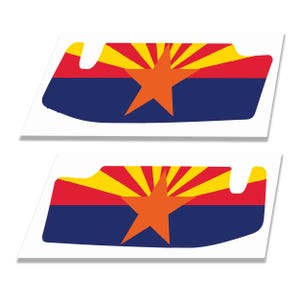 May include: Two identical vinyl decals featuring the Arizona state flag design. Each decal displays a copper-coloured star centred over thirteen alternating red and yellow rays on the top half, with a solid navy blue horizontal band on the bottom.