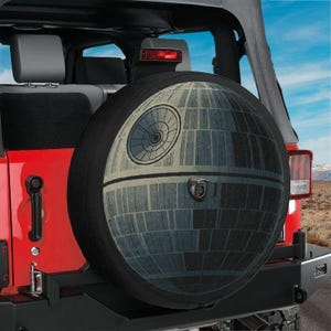 May include: A black spare tyre cover for a vehicle, featuring a detailed graphic print of a spherical space station with a large circular dish and paneling textures. The cover is mounted on the rear of a red vehicle with a visible backup camera.