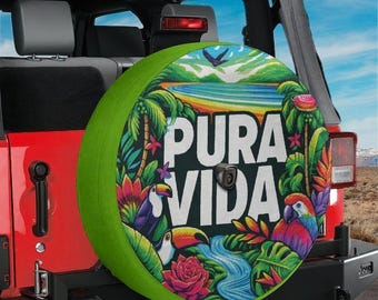 May include: A circular spare tire cover featuring a vibrant tropical scene with lush green foliage, colorful flowers, a toucan, a macaw, and a blue river. The text PURA VIDA is printed in large white letters across the center of the design.