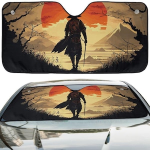 Op de afbeelding: Een rechthoekig zonnescherm voor de voorruit van een auto met een grafische illustratie van een figuur in traditionele kleding voor een grote oranje zon, een bergketen en bomen. Het ontwerp bevat twee doorzichtige zuignappen.