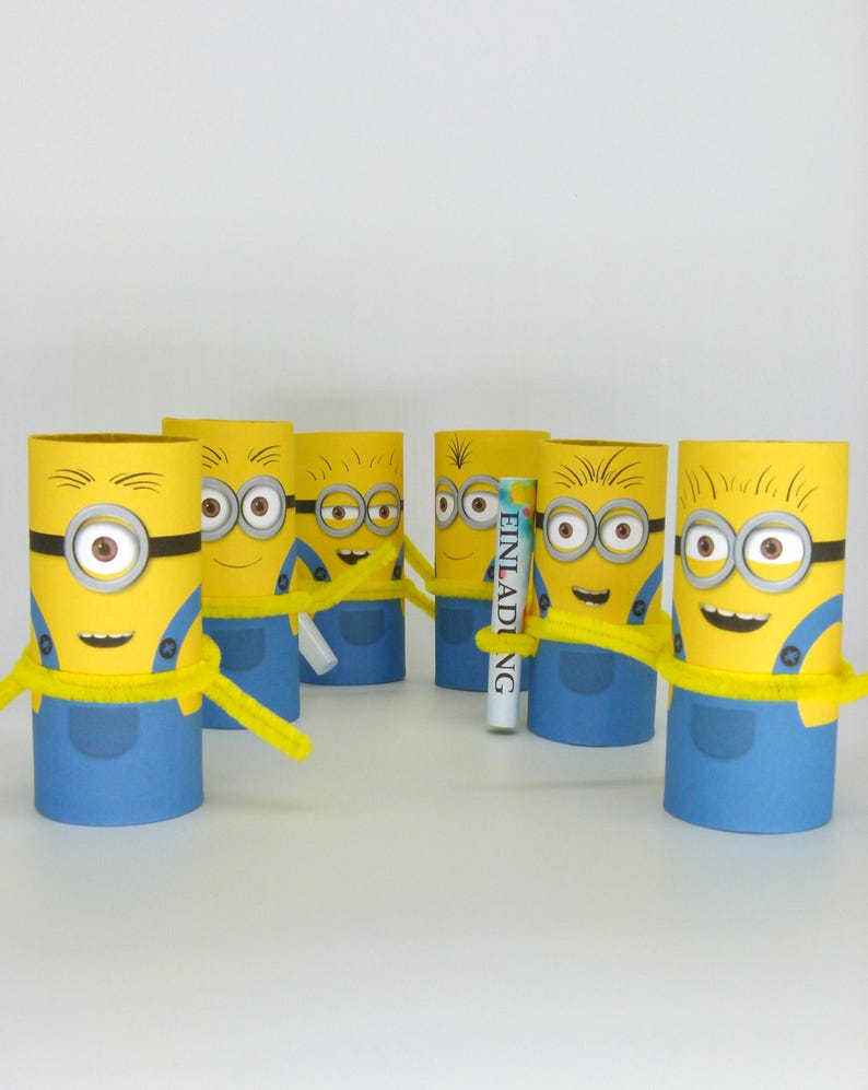 May include: Six yellow Minion characters made from cardboard toilet paper rolls. Each Minion has a blue jumpsuit, yellow goggles, and a black strap. The Minions are holding yellow pipe cleaners. One Minion is holding a white card with the word "Einladung" printed on it.