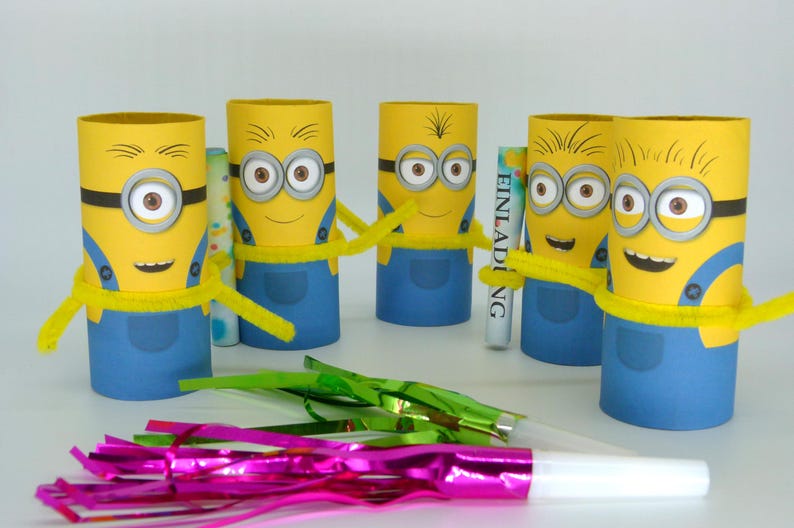 May include: Five yellow Minion character party favors made from cardboard toilet paper rolls. Each Minion has blue overalls, yellow hair, and googly eyes. The Minion in the center is holding a white card with the word "Einladung" printed on it.