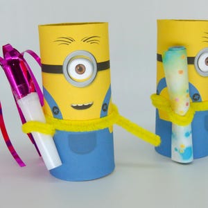 May include: Two yellow and blue Minion-themed cardboard tubes decorated with googly eyes, black lines, and a yellow pipe cleaner. One Minion holds a pink and white party blower with a streamer, and the other holds a blue and white rolled-up paper.