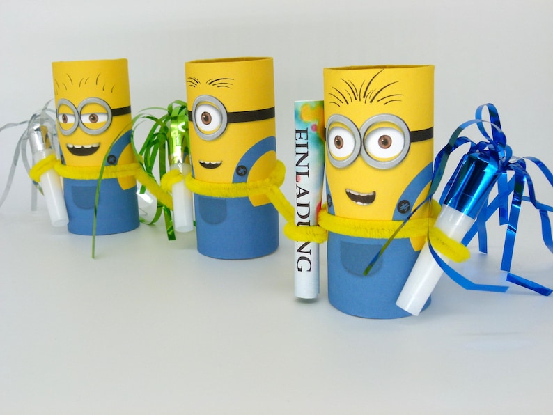 May include: Three yellow Minion-themed cardboard tubes decorated with blue overalls, googly eyes, and black goggles. Each tube has a different party favor inside, including a blue and silver party blower, a green streamer, and a white card with the word "Einladung" written on it.