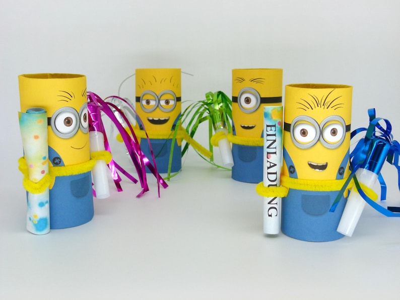 May include: Four yellow and blue Minion character party favor holders made from cardboard toilet paper rolls. Each holder has a yellow and blue Minion face with googly eyes and a yellow smile. Each holder has a different colored streamer attached to it. One holder has a white tube with the word "EINLADUNG" written on it.