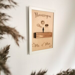 May include: A white framed wooden sign with the text "Haus Segen" and a sun, cloud, and arrow design. The sign also has the text "Mr. & Mrs." with hearts.