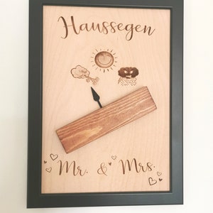 May include: A wooden plaque with a black frame, featuring the text "Haus Segen" and a weather vane with a sun, a cloud with wind, and a rain cloud. The plaque also includes the text "Mr. & Mrs." with hearts.