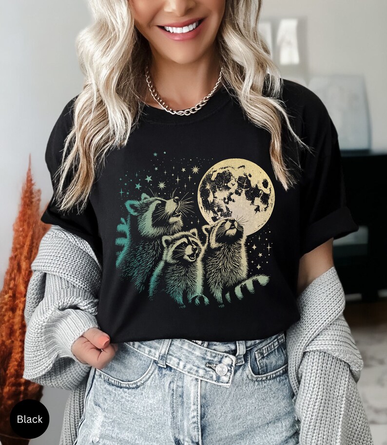 Op de afbeelding: Zwart T-shirt met een afbeelding van drie wasberen die naar een volle maan kijken met sterren op de achtergrond.