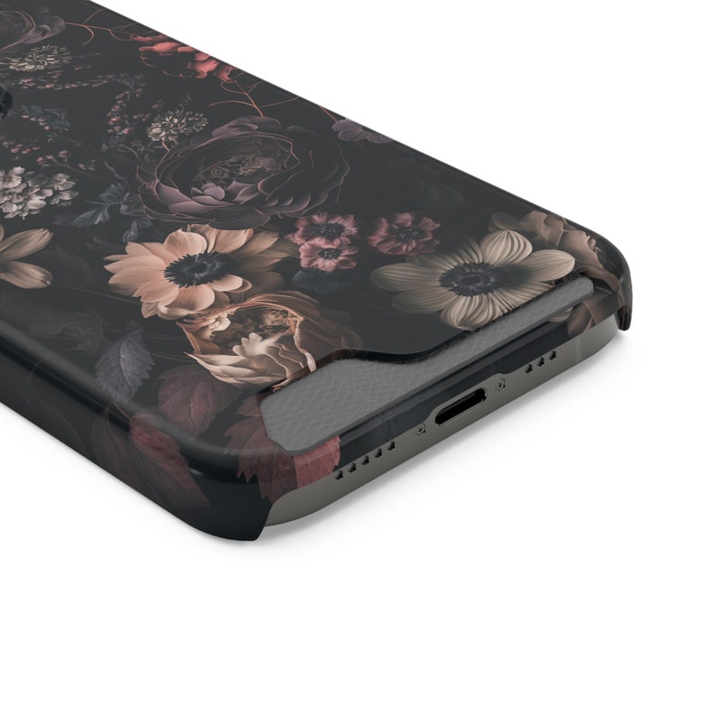 May include: A black phone case with a floral design featuring dark pink, white, and beige flowers. The case has a textured surface and a cutout for the phone's camera.