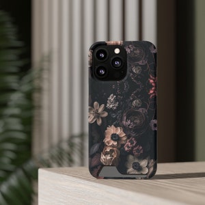 May include: A black phone case with a floral design featuring dark pink, white, and beige flowers. The case has a camera lens cutout with four small holes.