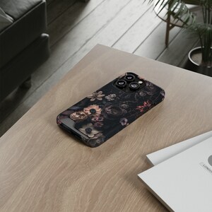 May include: A black phone case with a floral design. The case has a raised camera bump with three lenses.