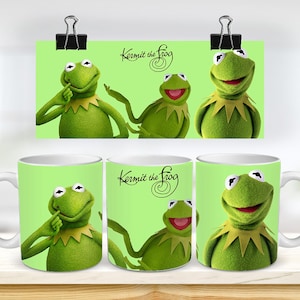 Puede incluir: Tres tazas de cerámica blanca con fondo verde y una imagen de dibujos animados de Kermit la Rana. El texto "Kermit the Frog" está impreso en la taza en una fuente cursiva negra.