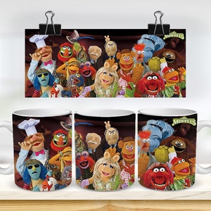 May include: Three white ceramic mugs featuring a colourful image of the Muppets characters. The mugs depict a variety of Muppets characters, including Kermit the Frog, Miss Piggy, and Fozzie Bear. The text "The Muppets" is printed on the mugs.